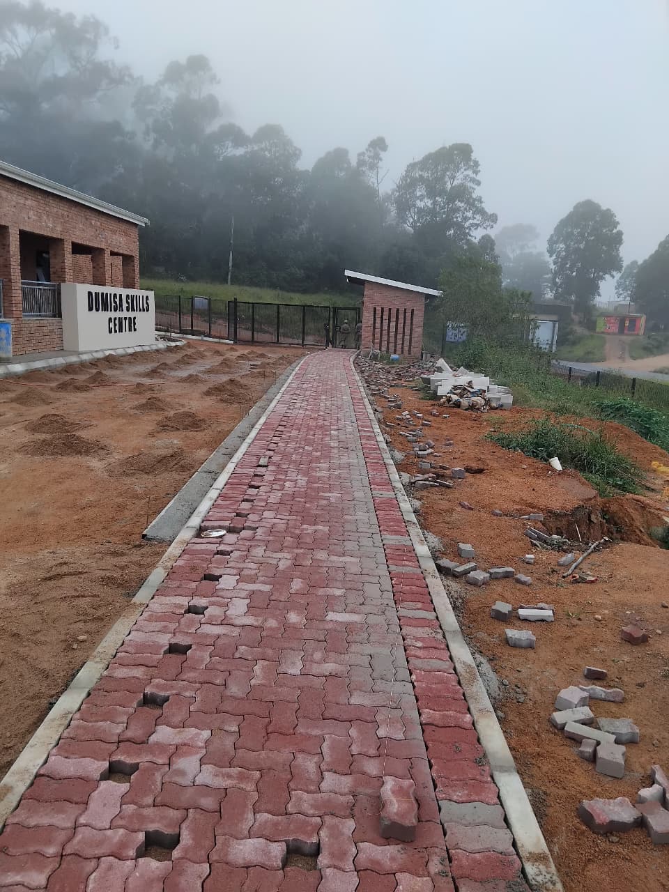 Red brick paved walkway leading toward a site entrance gate