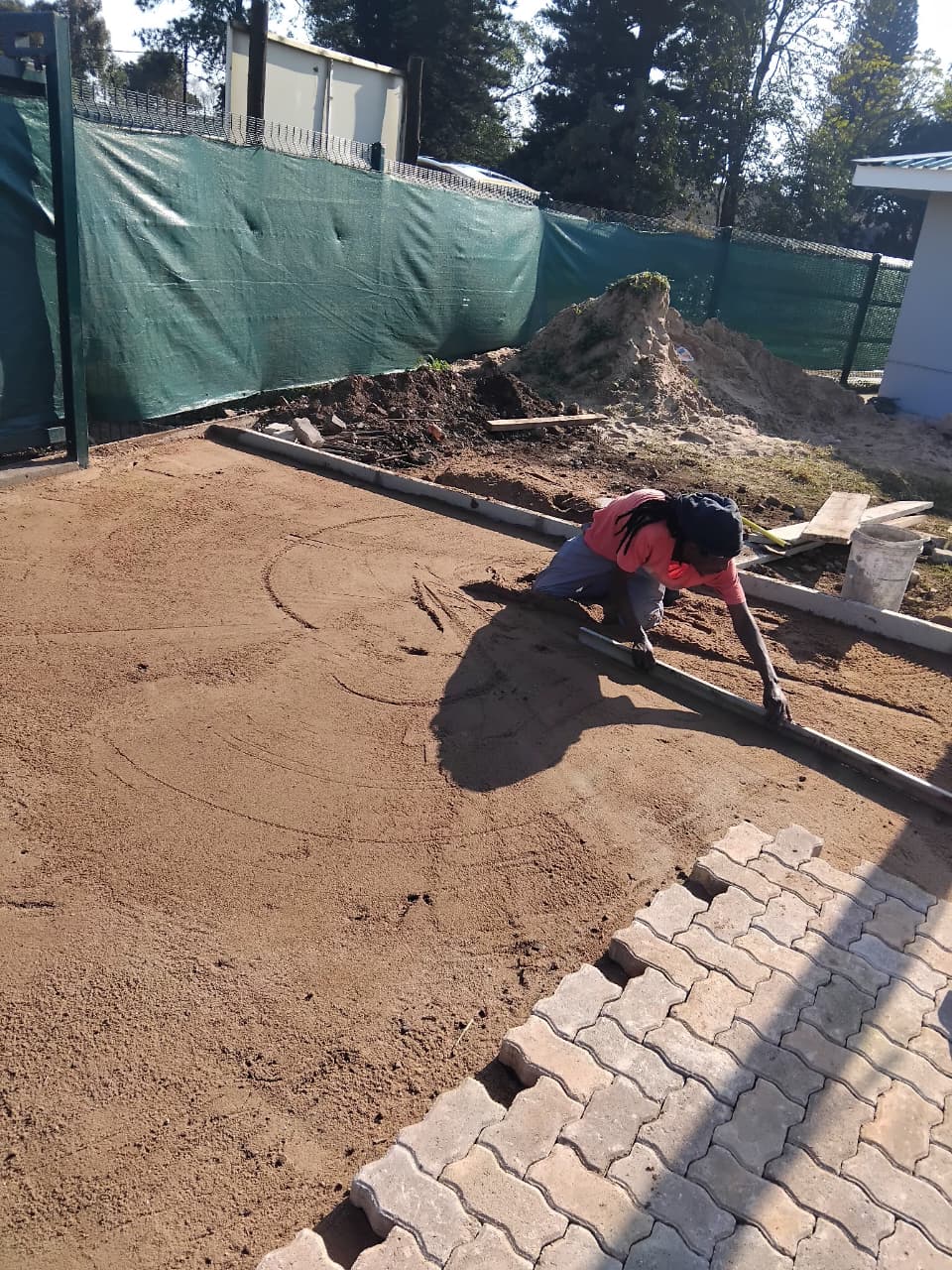 Worker screeding bedding sand level before laying interlocking pavers