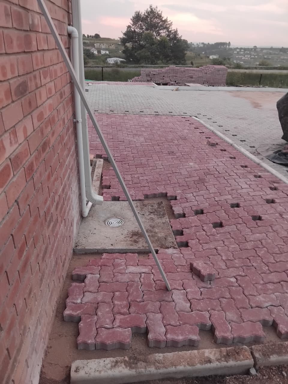 Red paving being laid around a drainage point beside a face brick wall